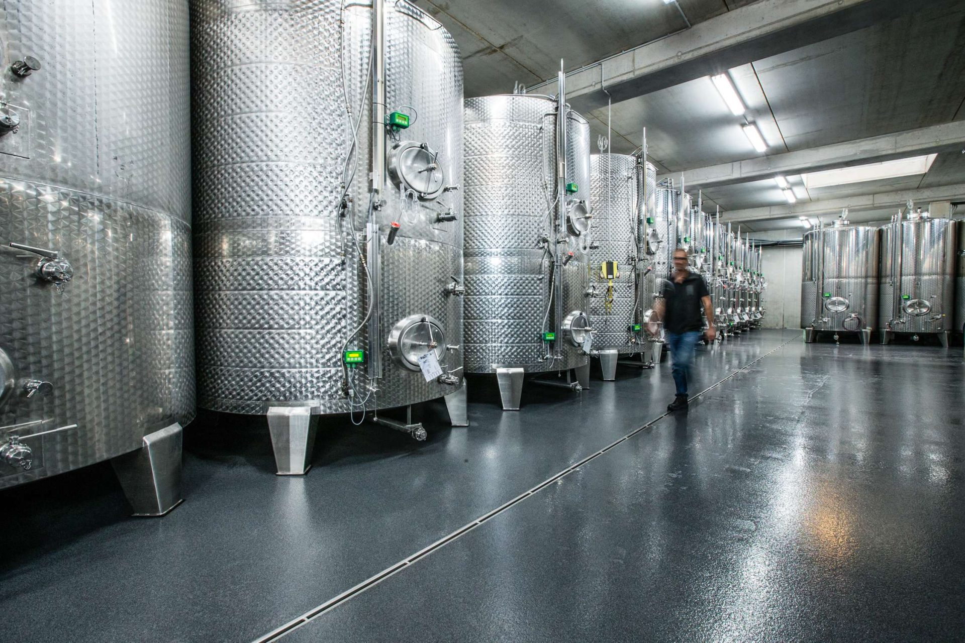 Mann läuft zwischen Edelstahltanks in Brauerei